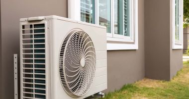 A white air conditioner mounted on the side of a house, blending with the exterior wall. 