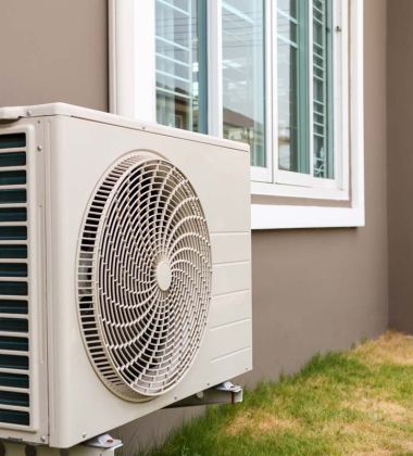 A white air conditioner mounted on the side of a house, blending with the exterior wall. 